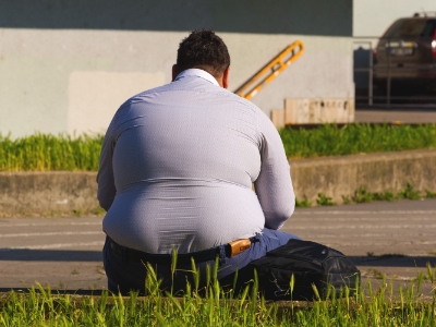 back of obese man in a blue sitting on the grass