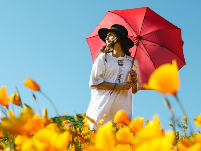 woman wearing a black hat using a red umbrella on a field of yellow flower